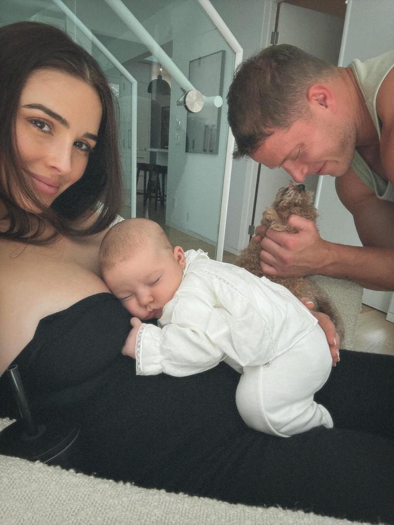 Olivia Frances Culpo and a baby napping on her chest, with a man holding a small dog in the background.