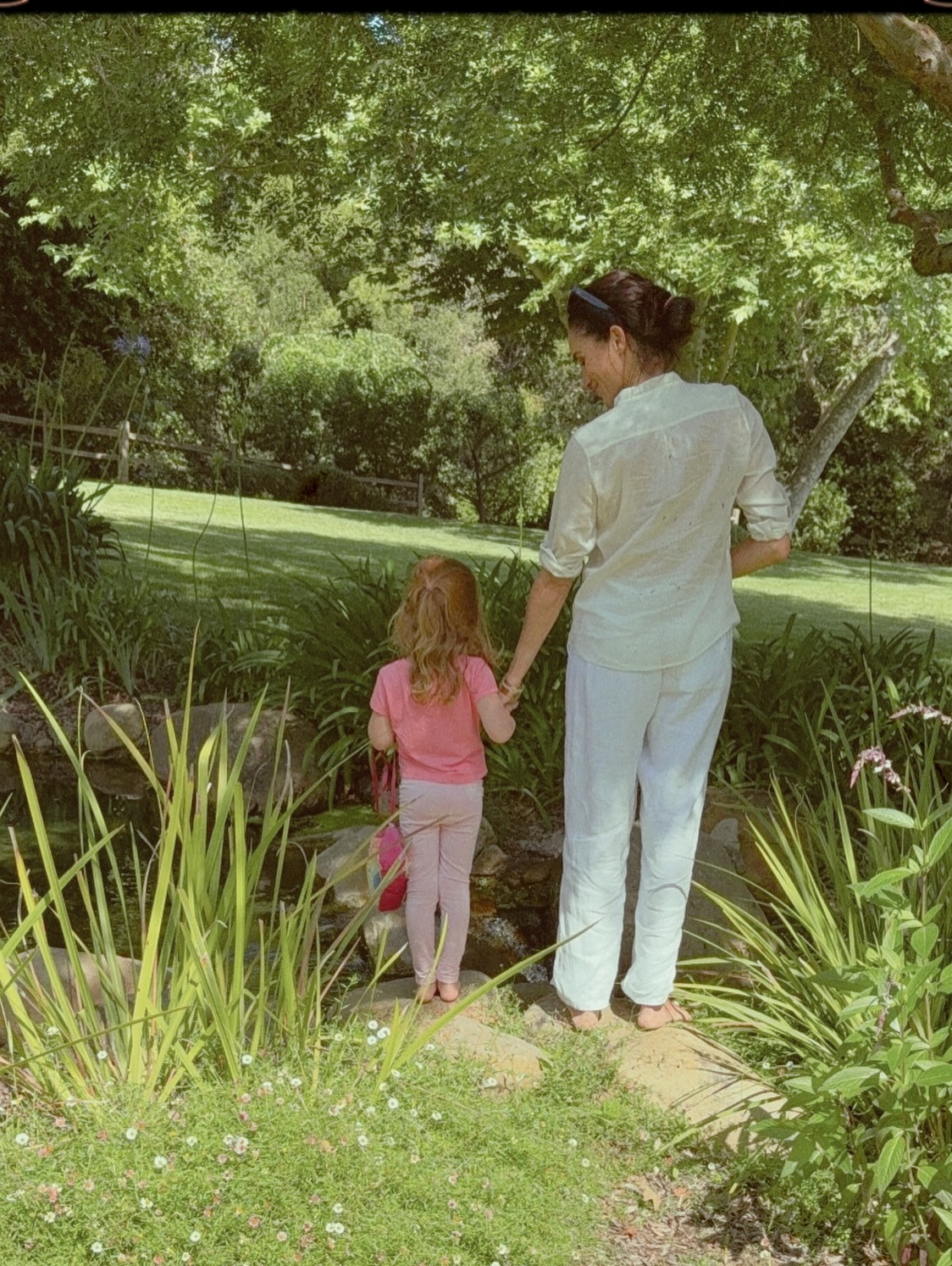 Meghan Markle holding hands with a young girl in a garden.