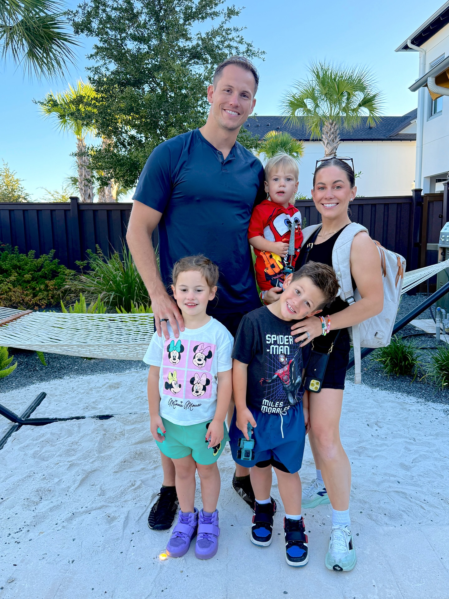 Shawn Johnson East and Andrew East posing with their three children, Drew, Jet, and Jett, in a sandy backyard.