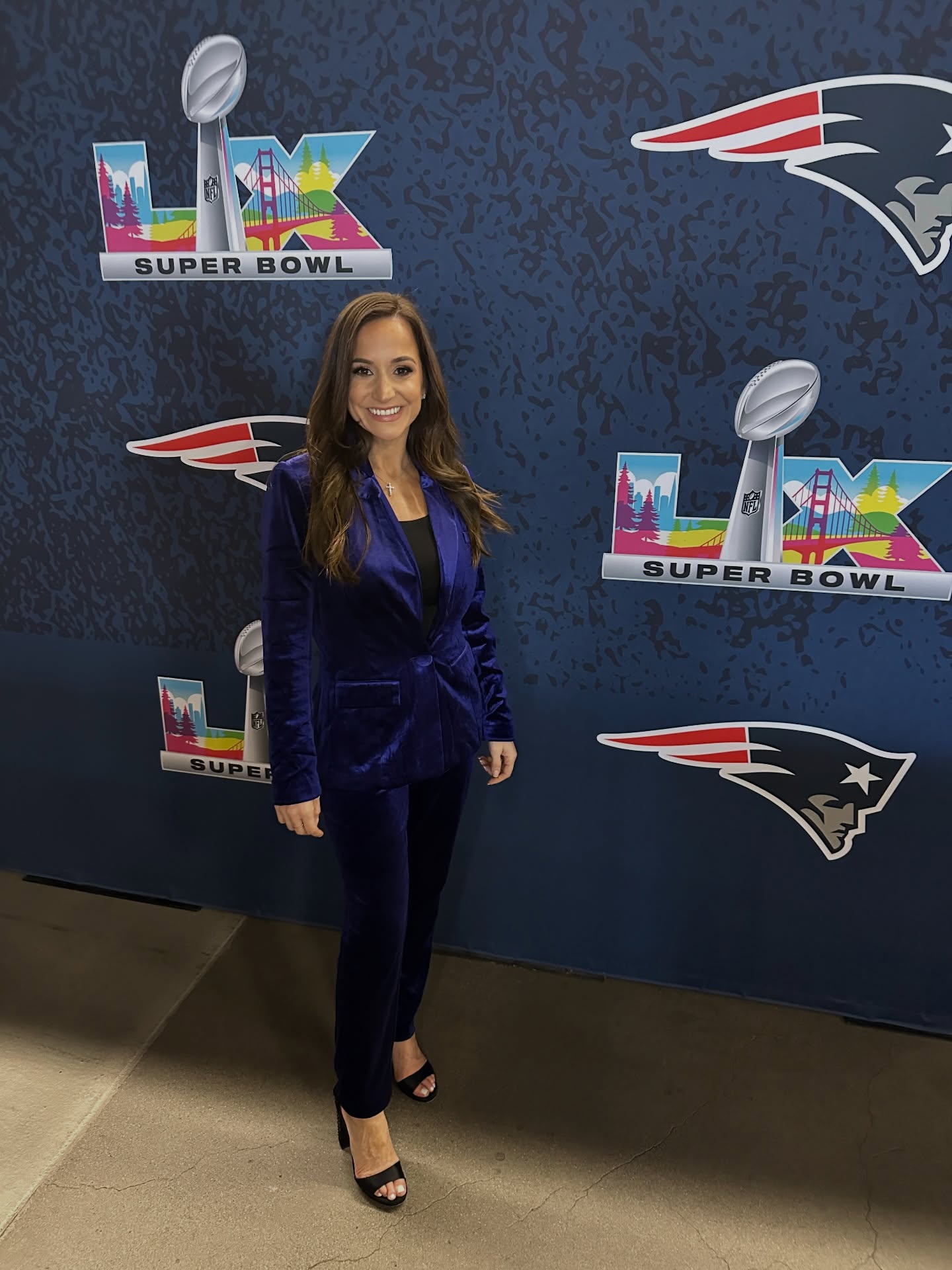 Dianna Russini posing in a blue pantsuit in front of a Super Bowl backdrop.