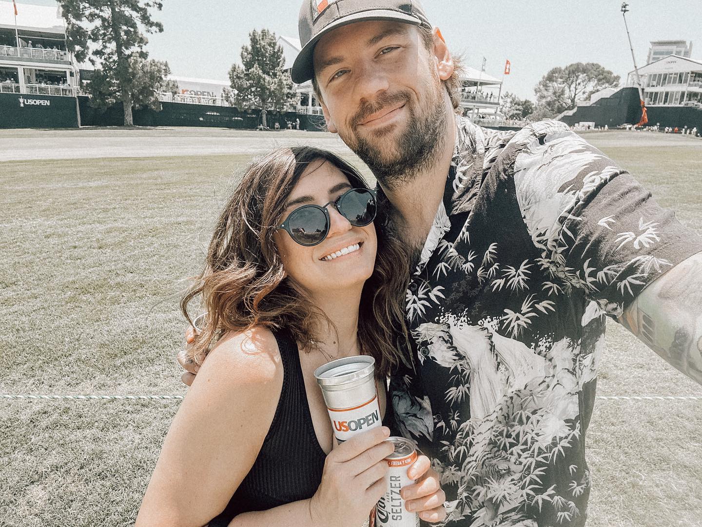 Fleur Shomo and Caleb Shomo smiling while holding drinks at the US Open.