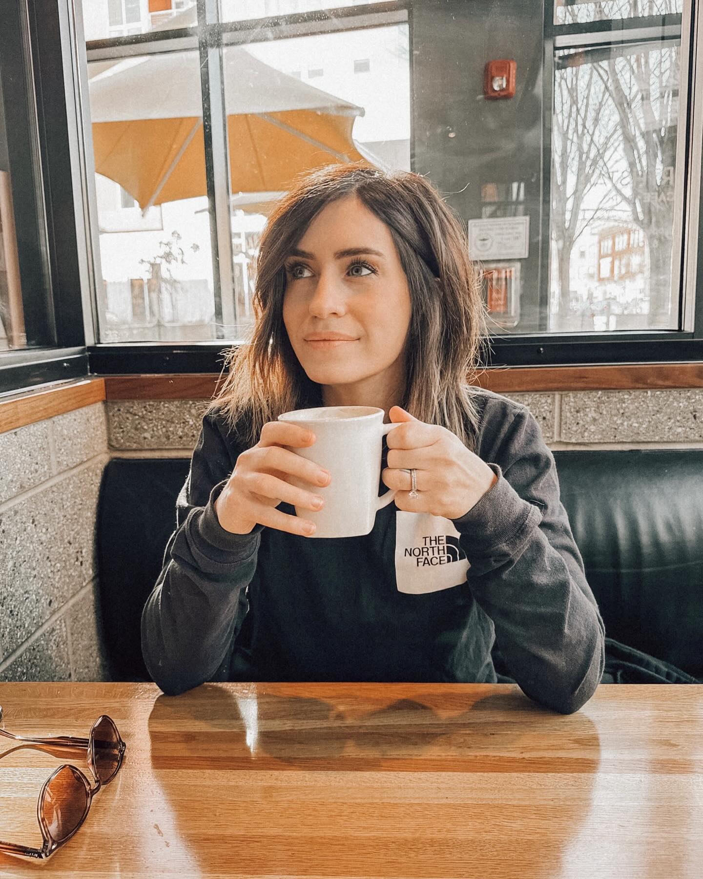 Fleur Shomo, Caleb Shomo's wife, holds a mug while sitting at a table with sunglasses.