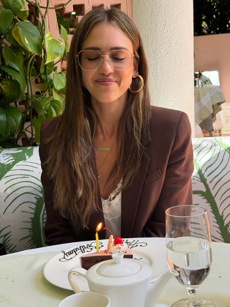 Jessica Alba closing her eyes to make a wish over a slice of chocolate birthday cake with a lit candle.