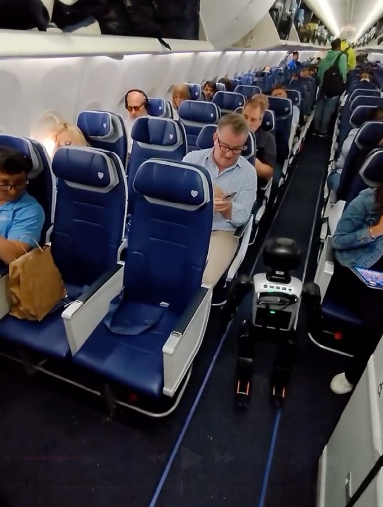 A small robot walks down the center aisle of an airplane