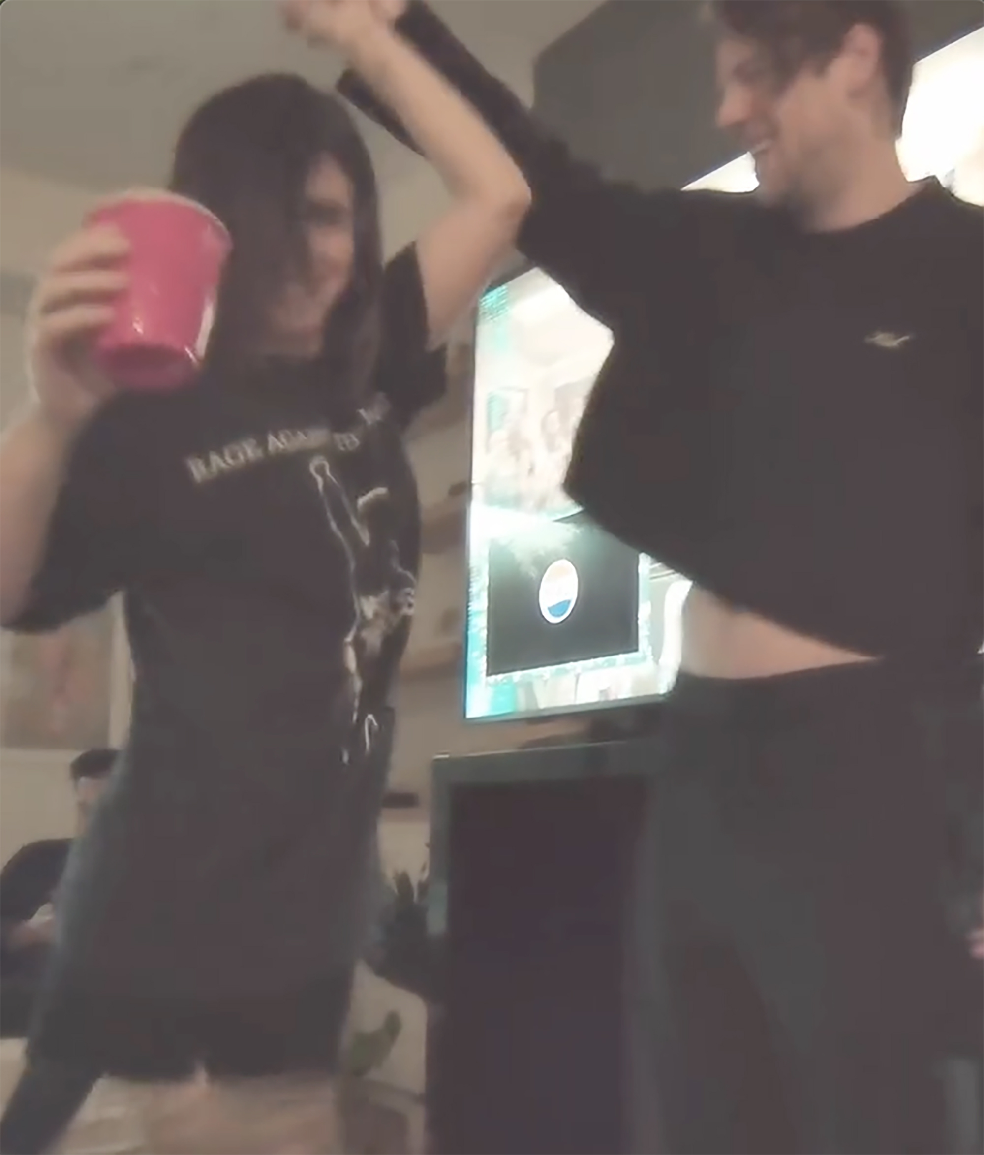 Caleb Shomo and his wife Courtney dancing happily, with Courtney holding a pink cup and Shomo showing his stomach.
