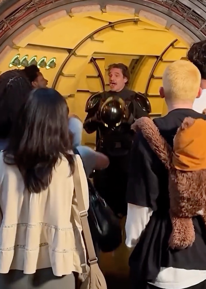 Pedro Pascal dressed as the Mandalorian holding a helmet in a crowd of fans.