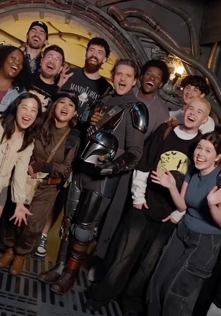 Pedro Pascal dressed as The Mandalorian with a group of smiling fans.
