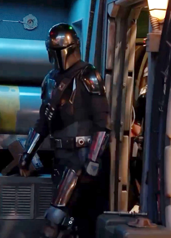 A person dressed as the Mandalorian from Star Wars, wearing black clothing, silver and bronze armor, and a helmet.