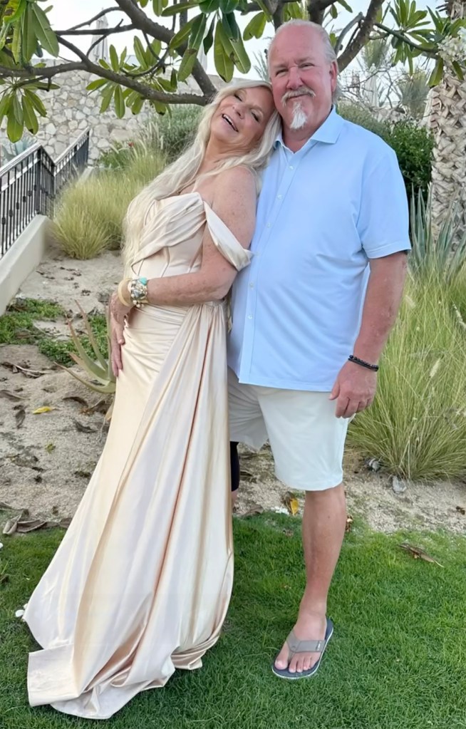Kimber and Darrell Sheets posing together outdoors, with Kimber in an off-the-shoulder golden dress and Darrell in a light blue polo shirt and white shorts.