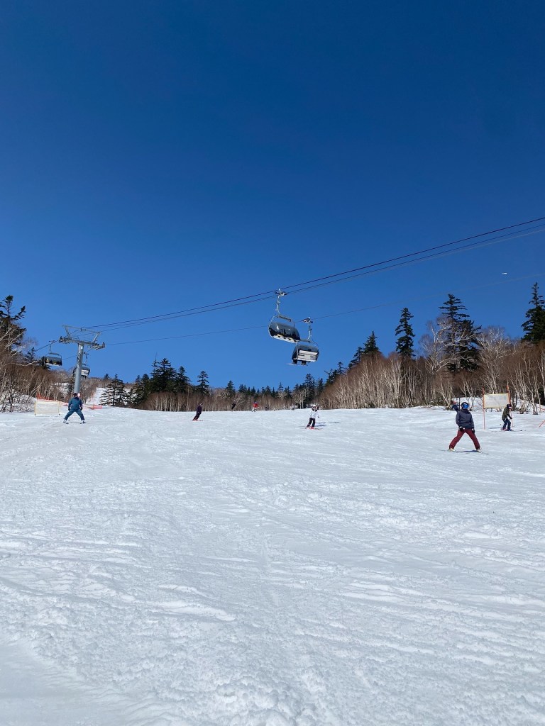 Sapporo Kokusai Skiing Resort with skiers on a slope and ski lifts overhead.