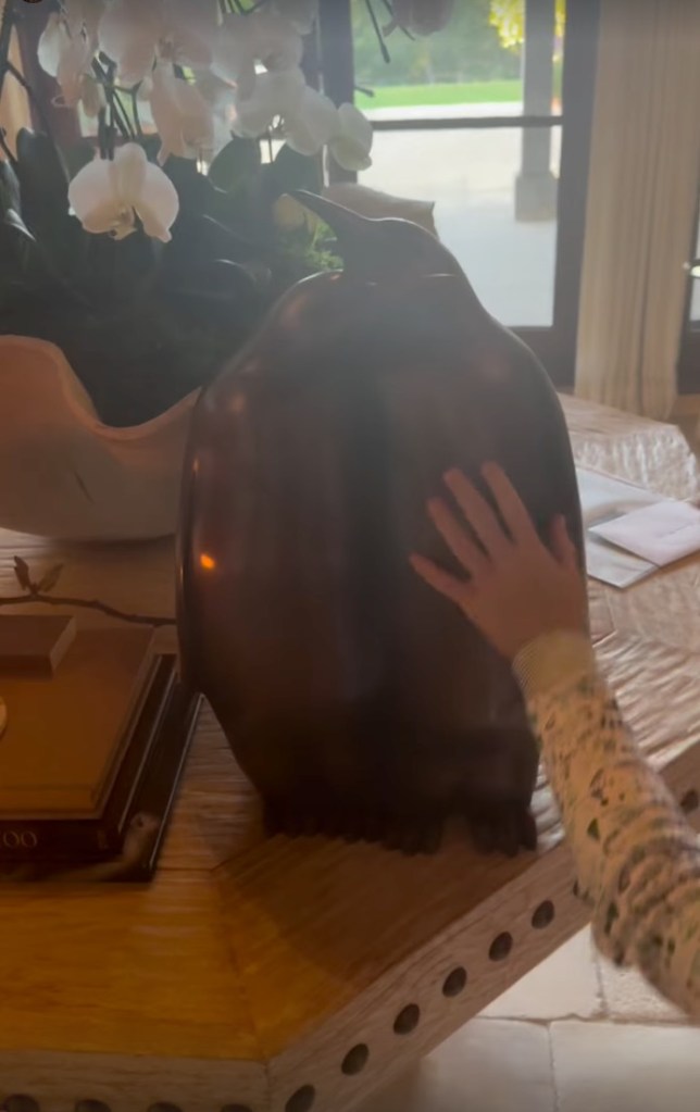 Child's hand touching a large, dark penguin sculpture next to white orchids.