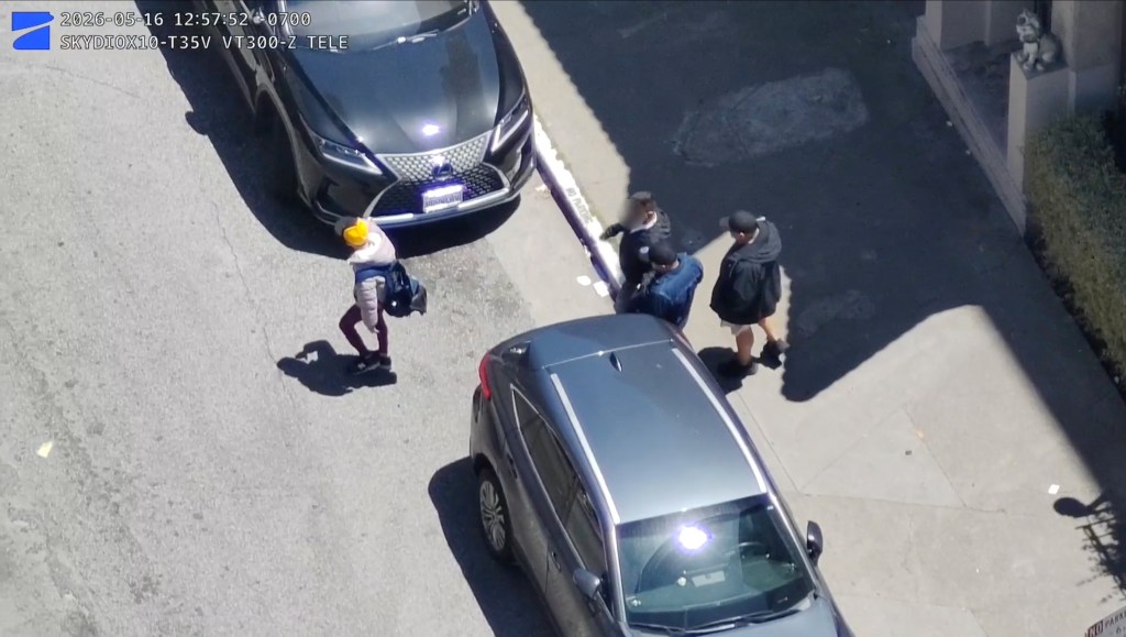 A high-angle view of three suspects following a victim on the street between parked cars.