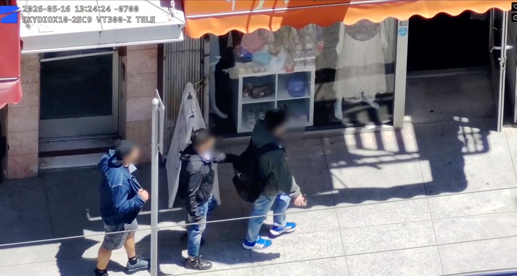 CCTV footage of three individuals on a sidewalk with blurred faces, one appears to be pickpocketing another.