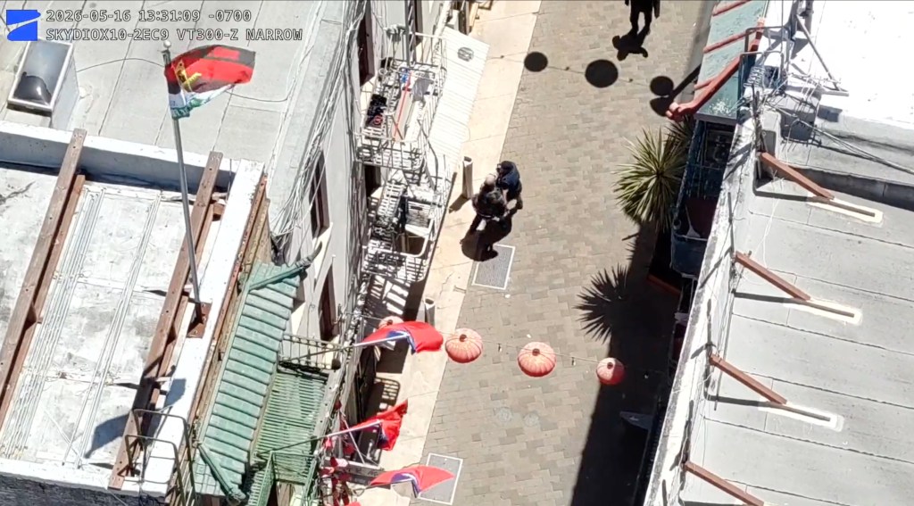 Aerial view of a police officer detaining a suspect on a paved alleyway in Chinatown.