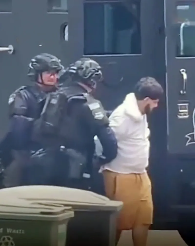Joaquin Escoto being arrested by two tactical officers.