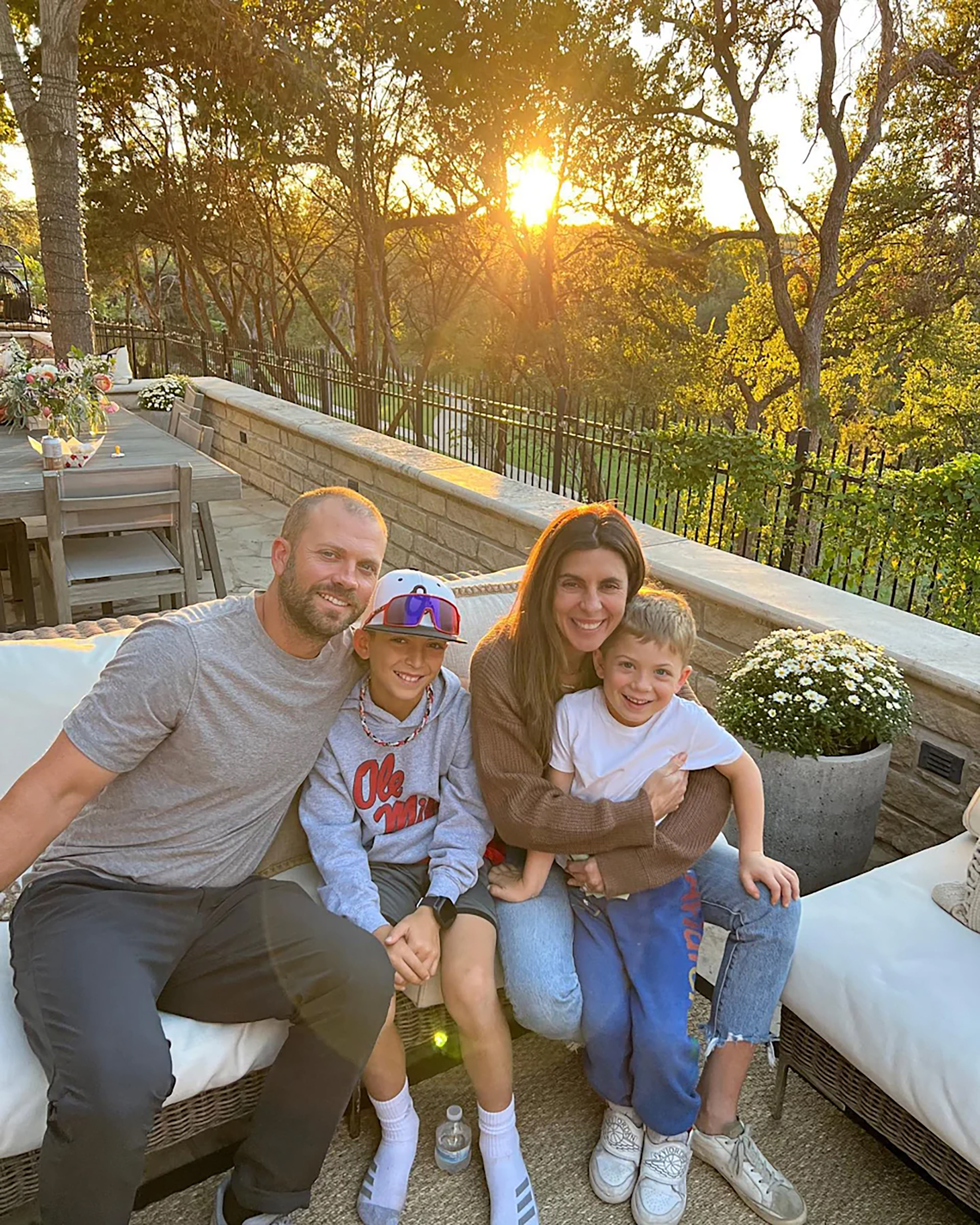Jamie-Lynn Sigler with her husband and two sons sitting on an outdoor sofa.