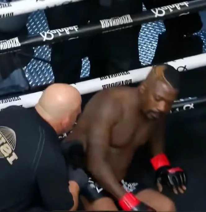 A referee assisting Ray J who is sitting in the corner of a boxing ring after being knocked out.