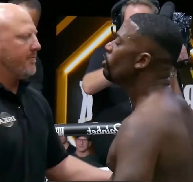 A boxing referee talking to Ray J inside the ring.