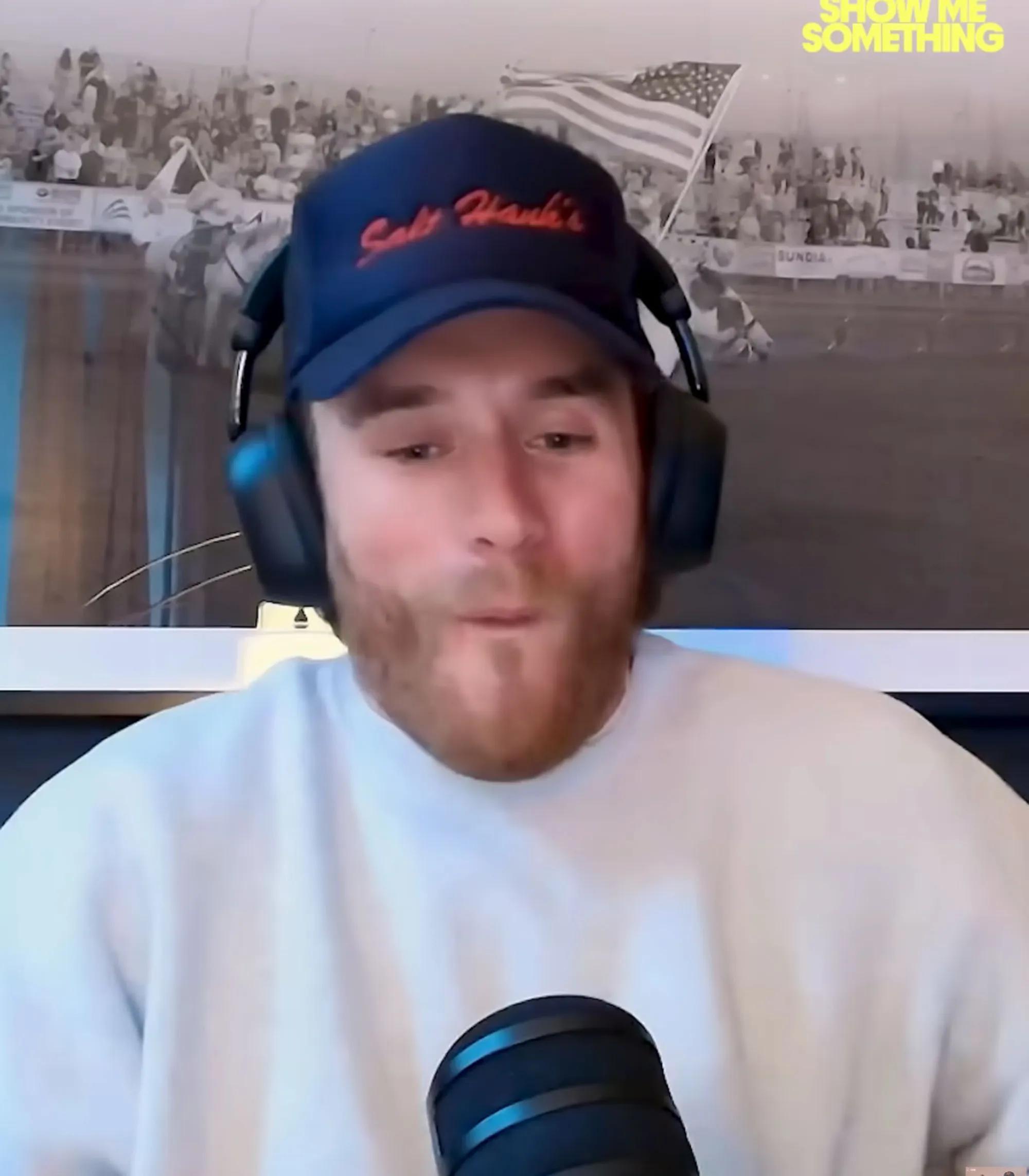 West Wilson wearing a blue baseball cap and headphones, speaking into a microphone.
