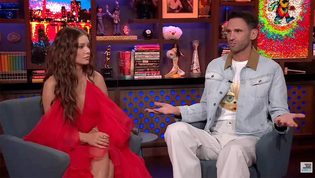 Carl Radke speaking on Watch What Happens Live with a woman in a red dress beside him.