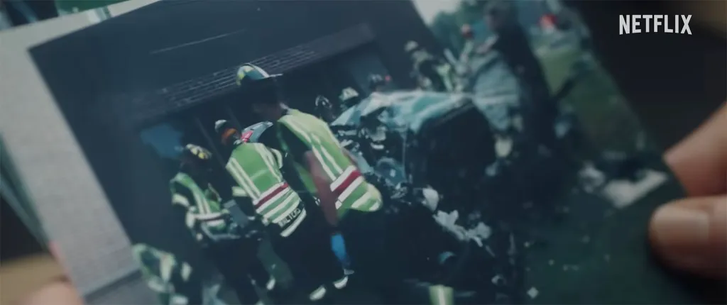 A photo held by a hand shows emergency responders in green vests at the scene of a vehicle crash.