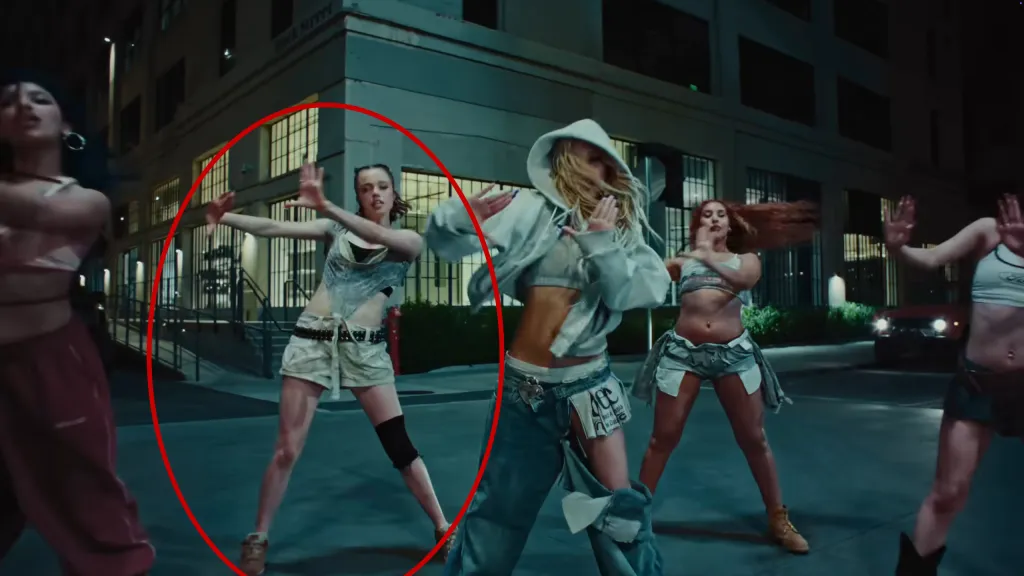 Shiloh Jolie-Pitt dancing in a music video, wearing a tattered top and shorts.