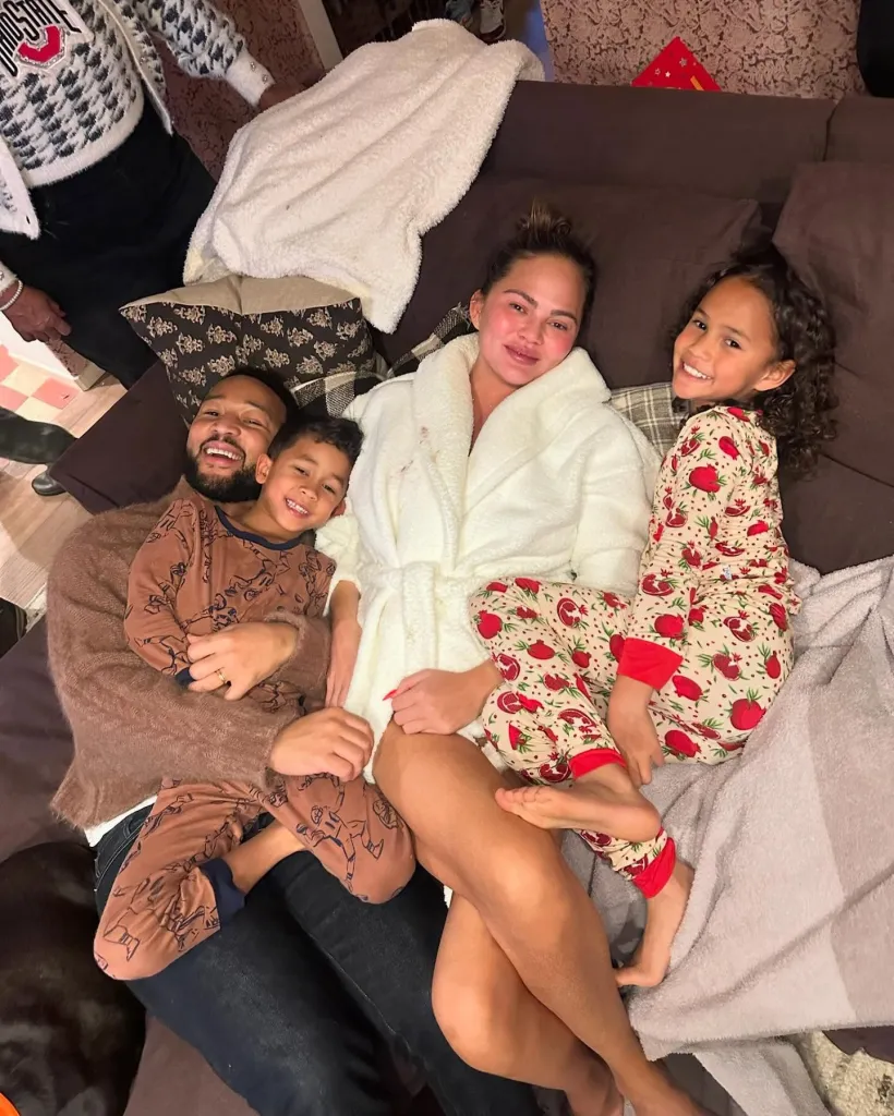Chrissy Teigen and John Legend with their two children, all smiling, on a couch.