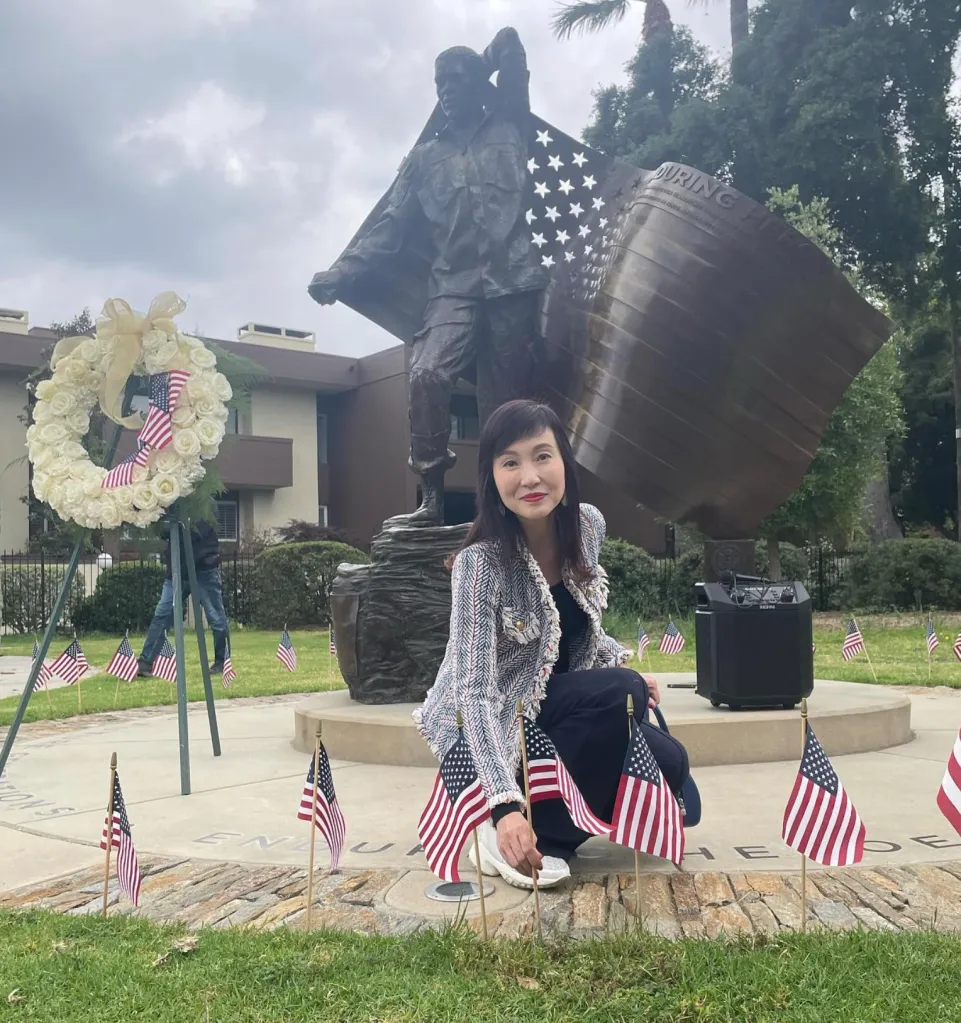 Yvonne Yiu kneeling by a statue with American flags and a white rose wreath.