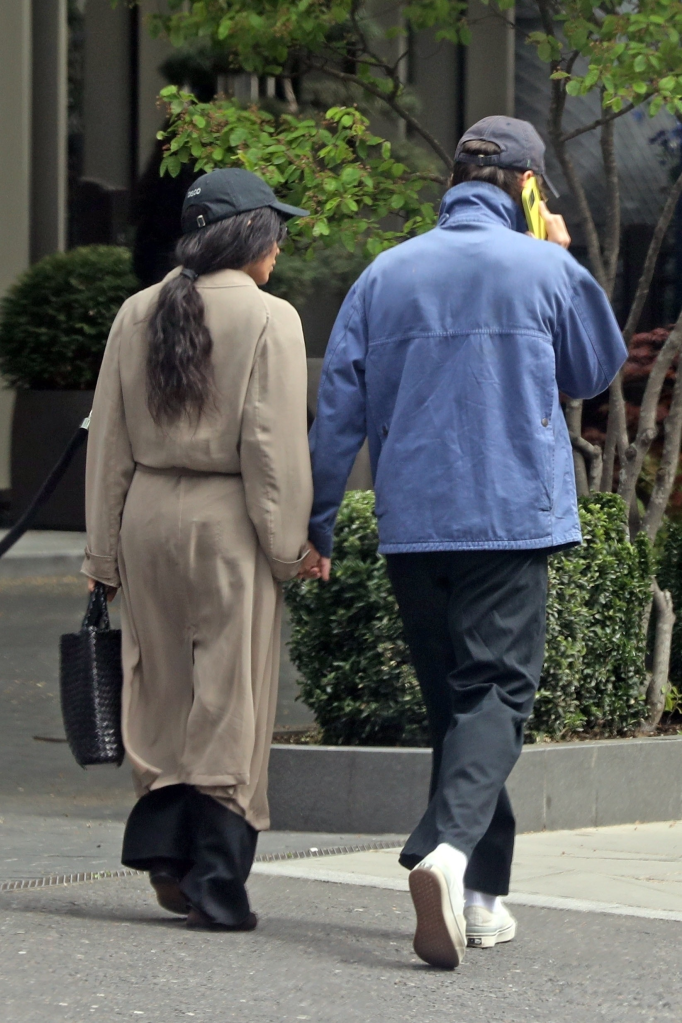 Harry Styles and Zoe Kravitz holding hands and walking away, seen from behind.