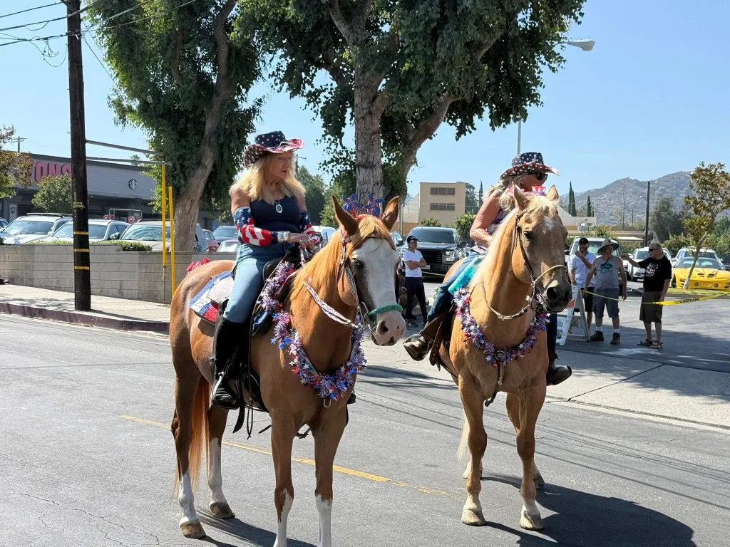 Two women riding horses decorated with red, white, and blue garlands and hats.