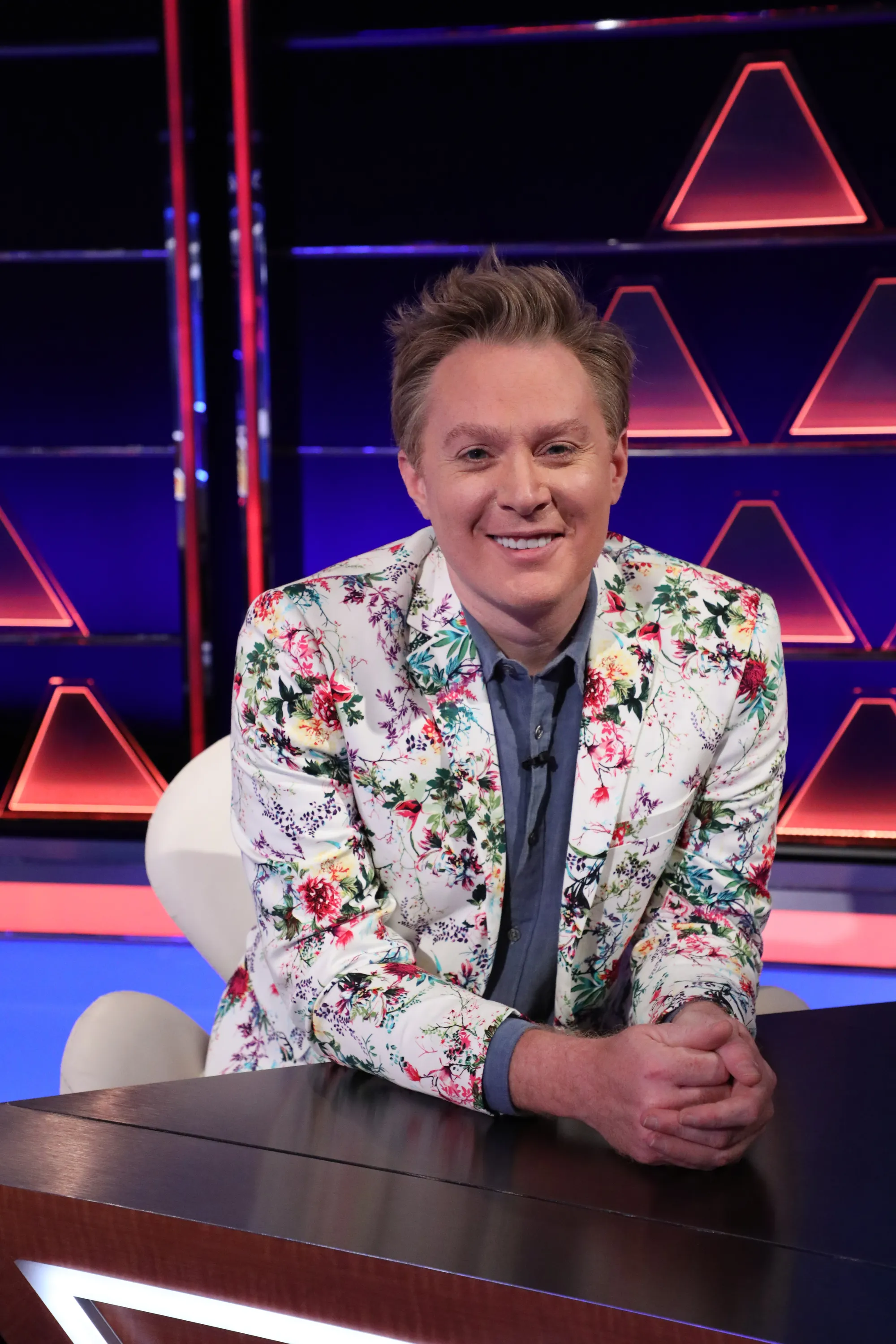 Clay Aiken seated at a table on the set of The $100,000 Pyramid.