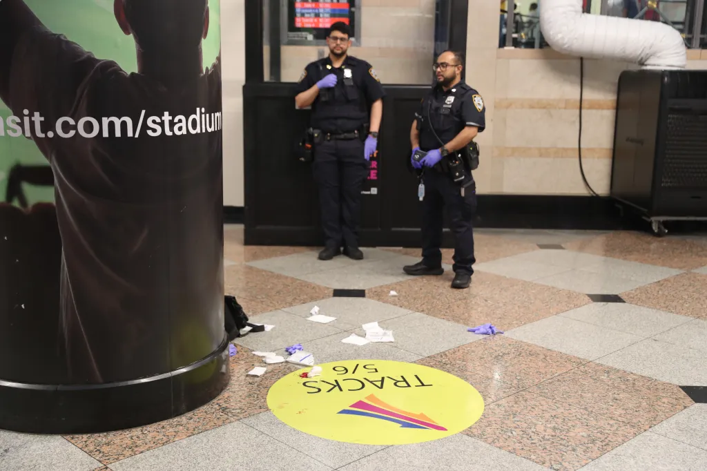 Two police officers stand near bloodied debris on the floor, including a yellow 