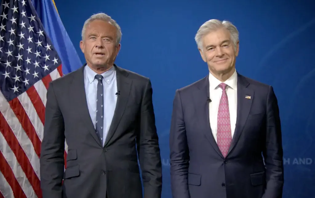 Robert F. Kennedy Jr. and Dr. Mehmet Oz standing side-by-side in front of American and Ukrainian flags.