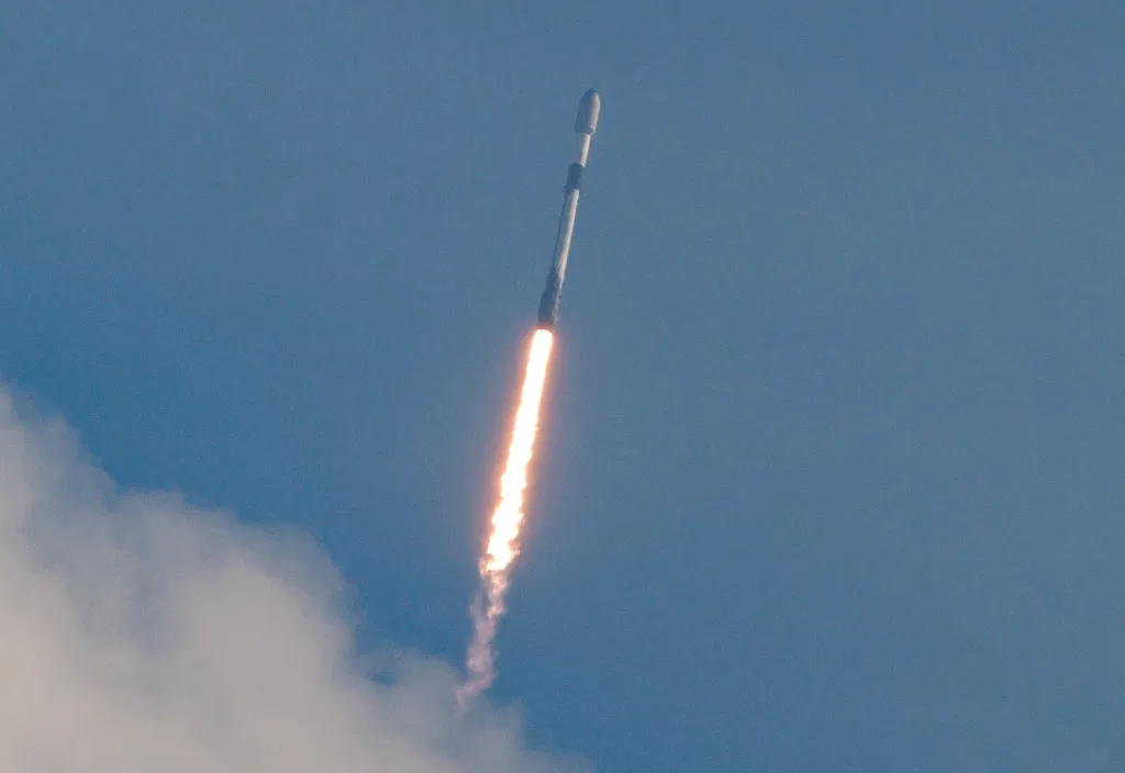 A SpaceX Falcon 9 rocket launching into the sky, its engines producing a bright orange plume of fire and smoke.