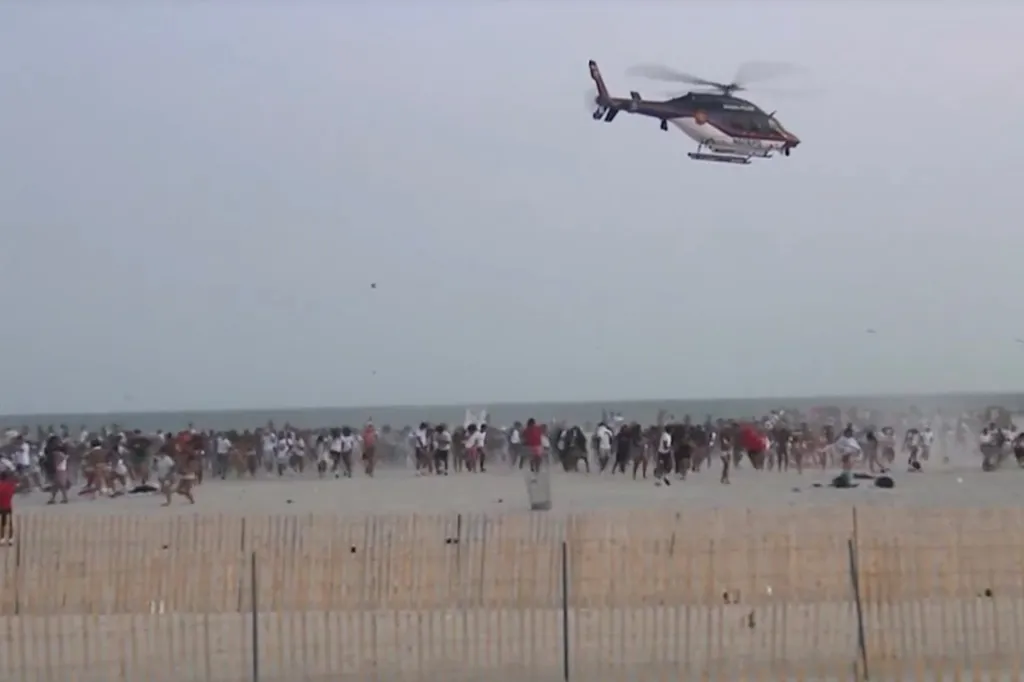 Police helicopter flying over a large gathering of people running on a beach.