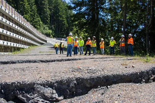 Caltrans staff inspecting the landslide activity at Last Chance Grade, with a retaining wall and forest in the background.