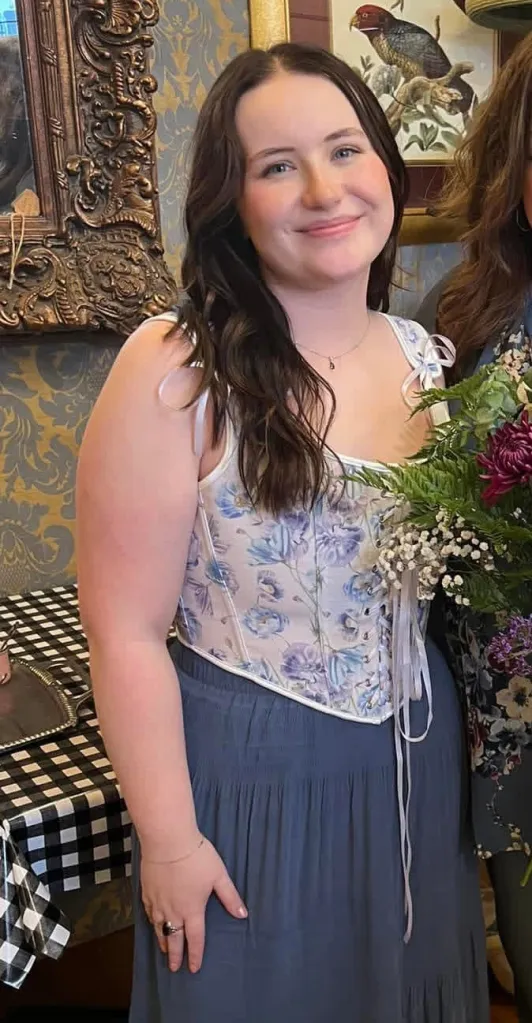 A smiling woman in a floral corset and blue skirt.