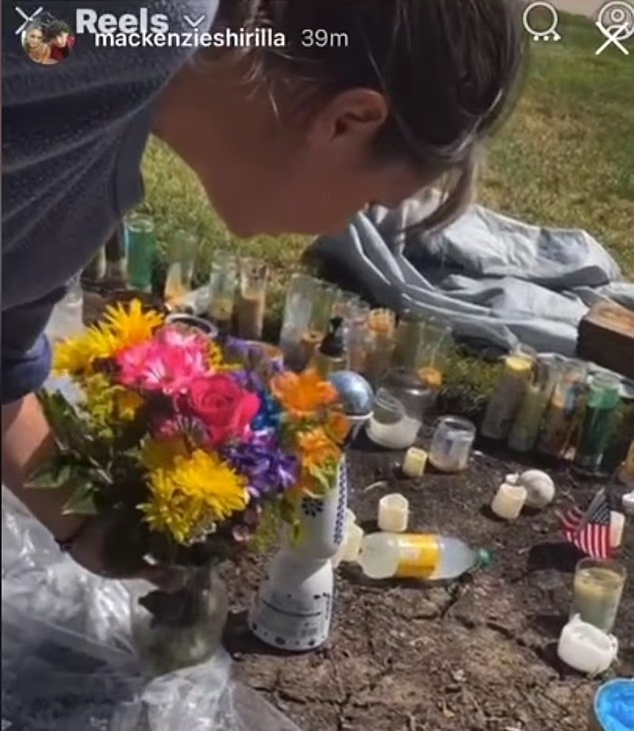 A woman placing flowers at a roadside memorial with candles and American flags.