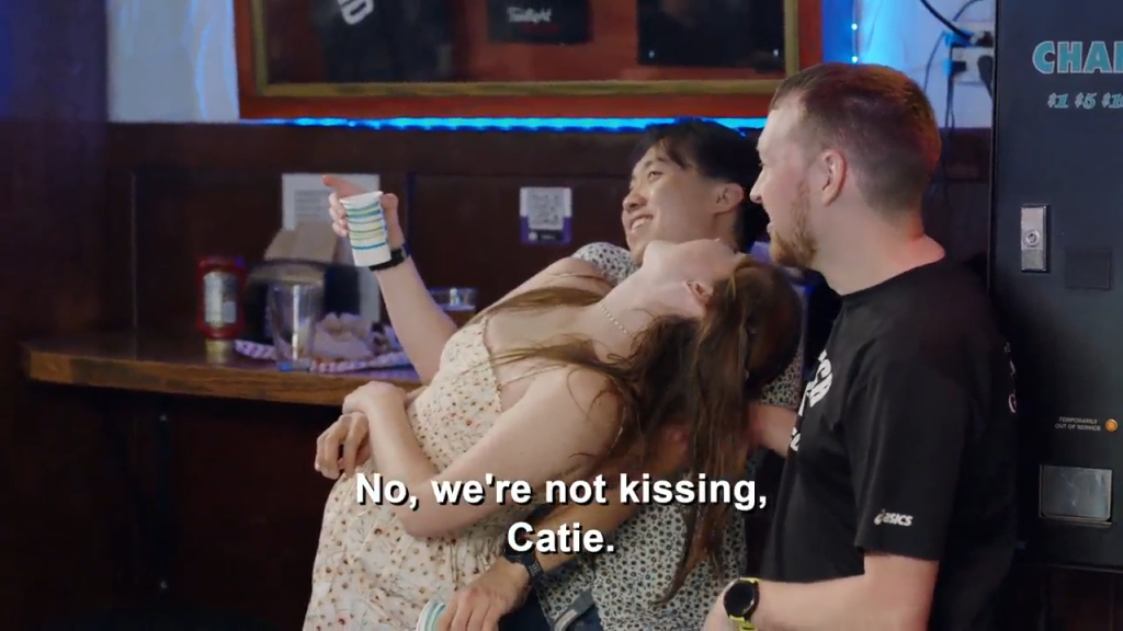 Catie tries to kiss a guy as another man watches.