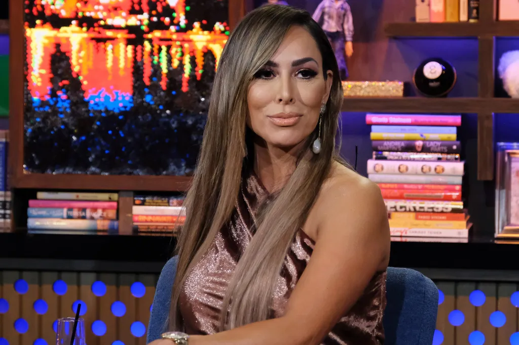 Kelly Dodd sits in a brown, sparkling top with long brown hair, looking slightly to her left.