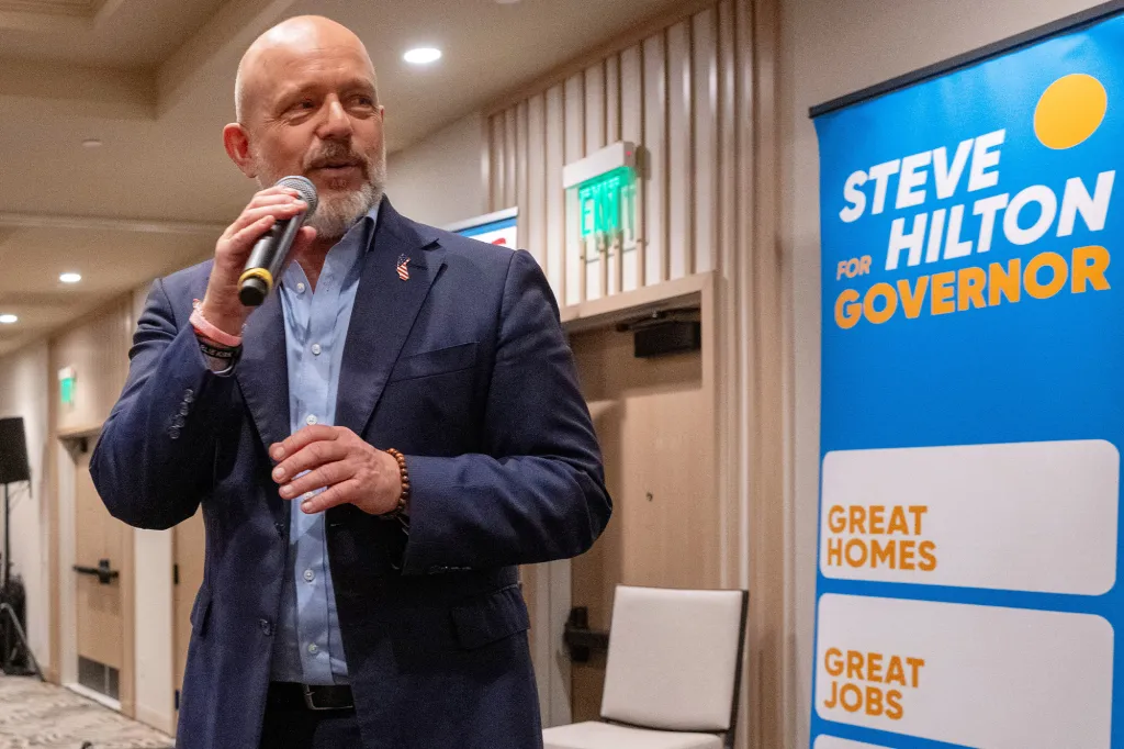 Steve Hilton speaks into a microphone at a campaign event, next to a 