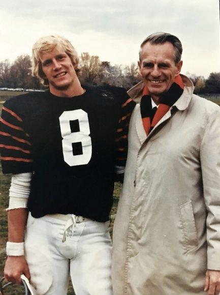 A young man in a football uniform with a number 8 on his shirt next to an older man in a coat and scarf.