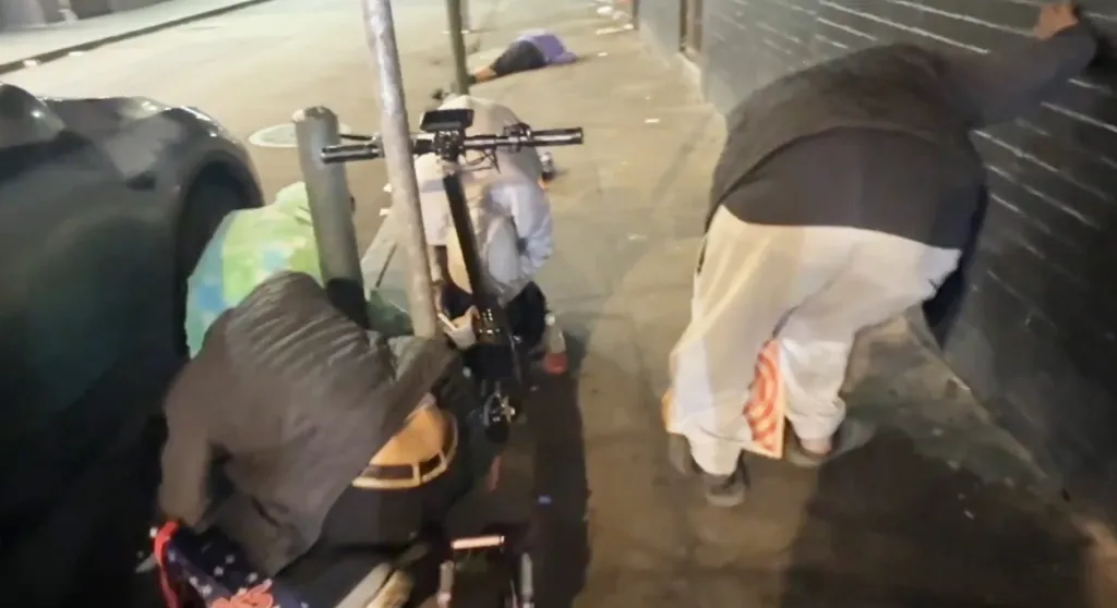 People on a street, with one lying on the ground.