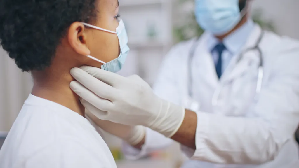Doctor checking a child's lymph nodes, both wearing face masks.