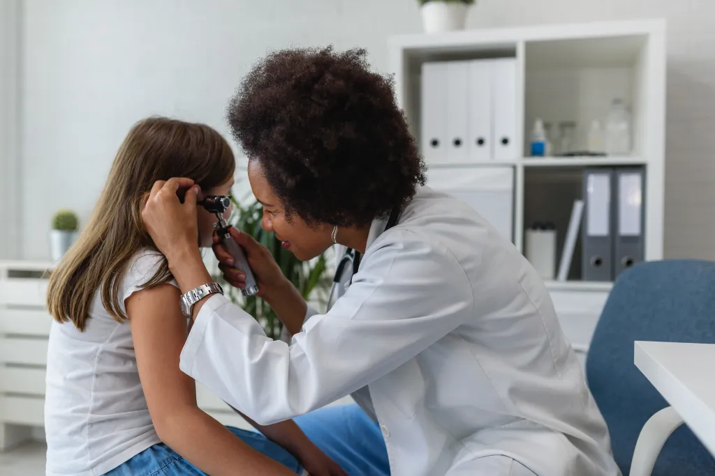 African American female doctor examining a child's ear with an otoscope.