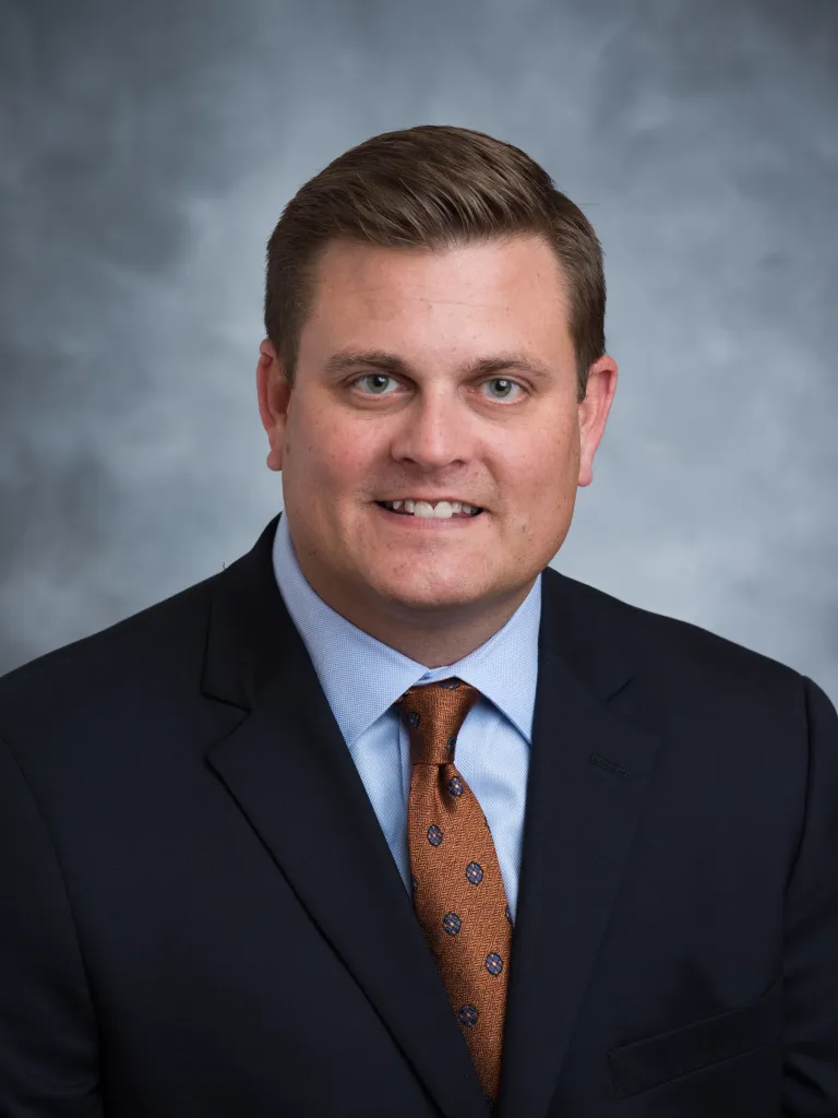 Headshot of a man in a suit and tie smiling.