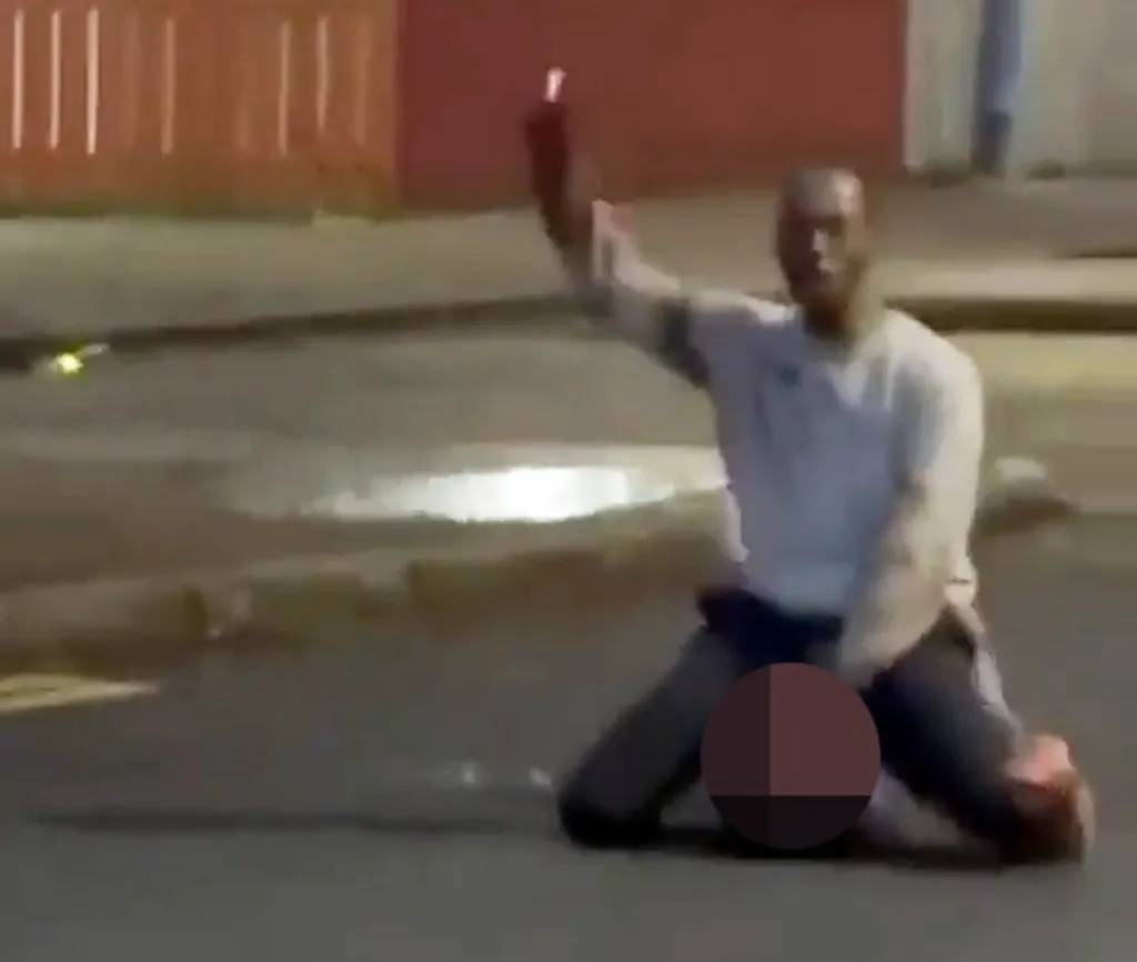 A man kneels on the ground with one arm raised in the air, holding a red flare.