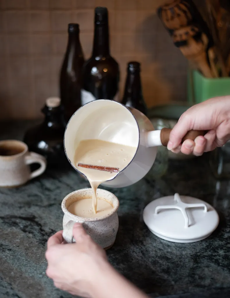 A hand pouring a creamy drink into a mug