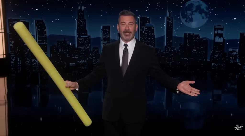 Jimmy Kimmel holding a yellow pool noodle on stage.