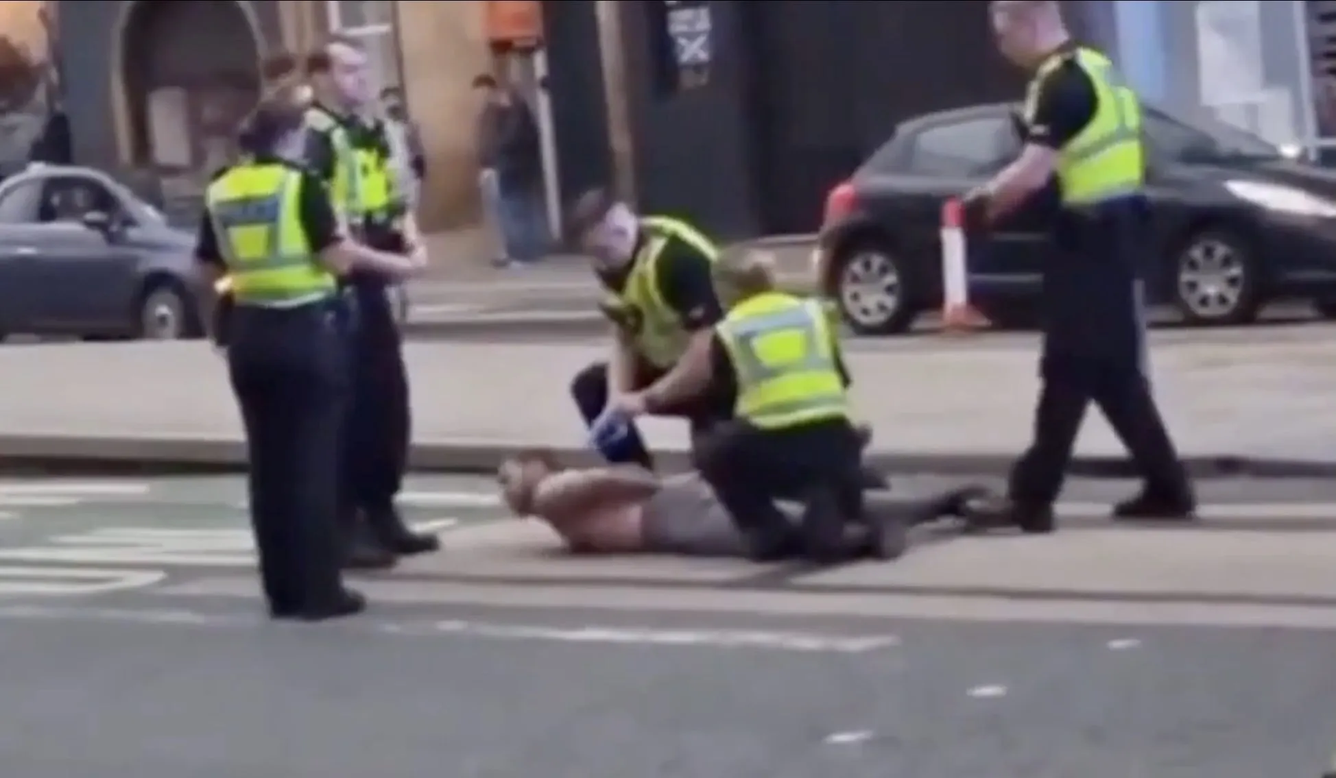 Police officers detaining a shirtless man on the street.